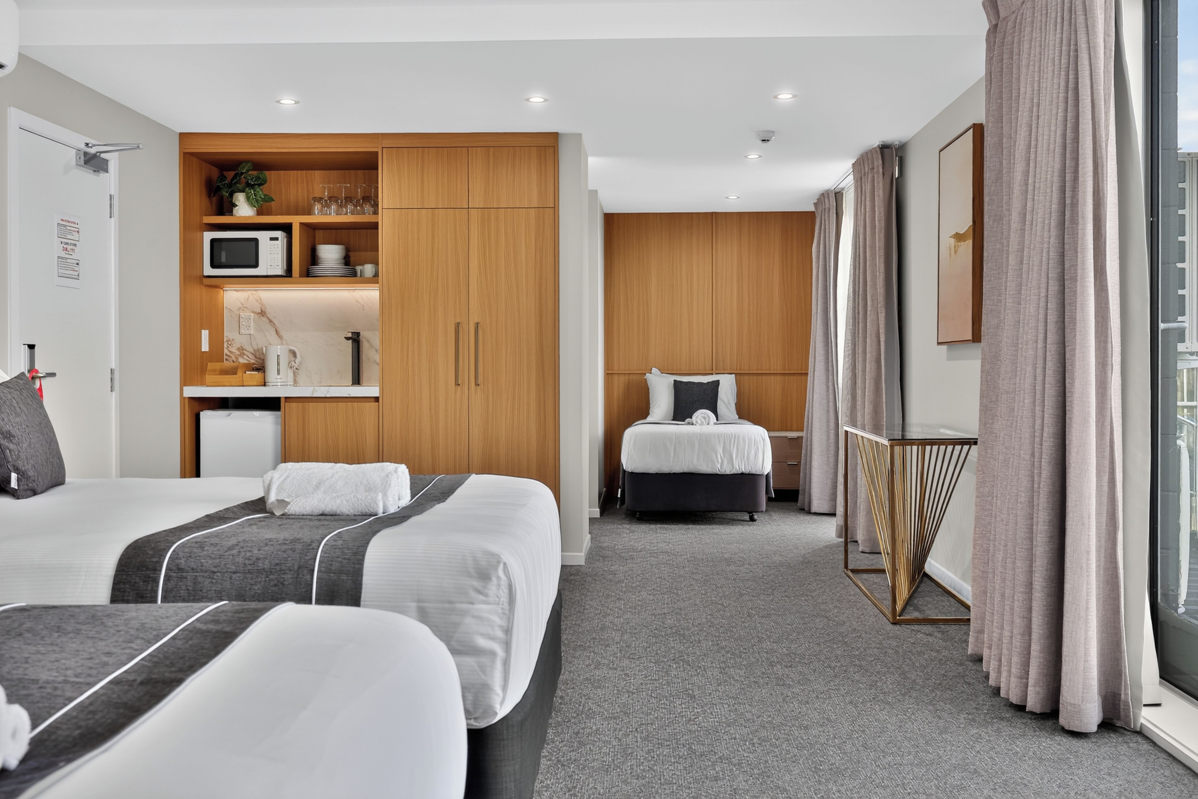 Habitación de hotel con dos camas, kitchenette, baño y un ventanal con cortinas.