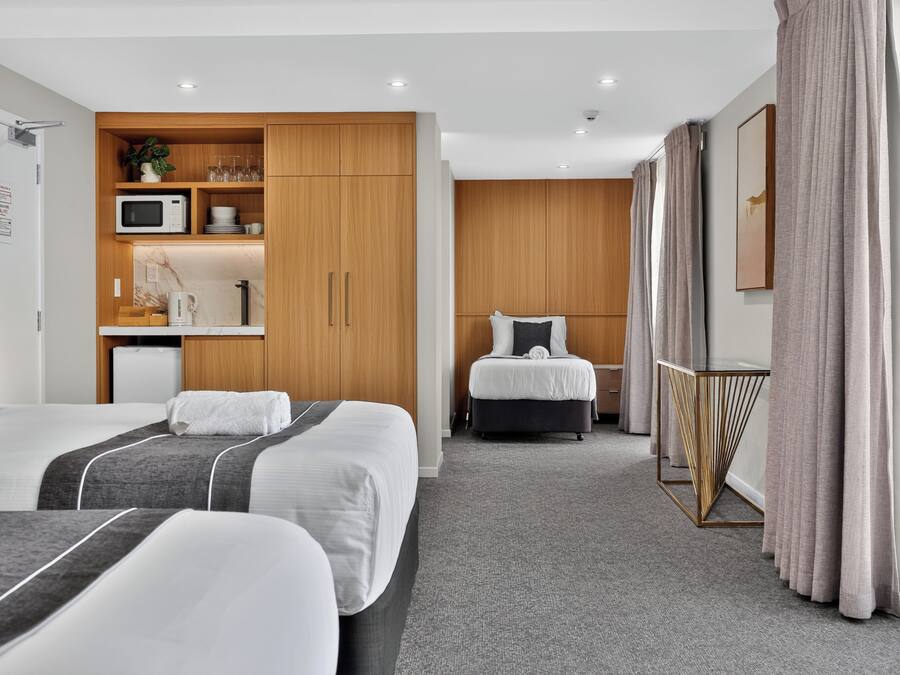 Habitación de hotel con dos camas, kitchenette, baño y un ventanal con cortinas.