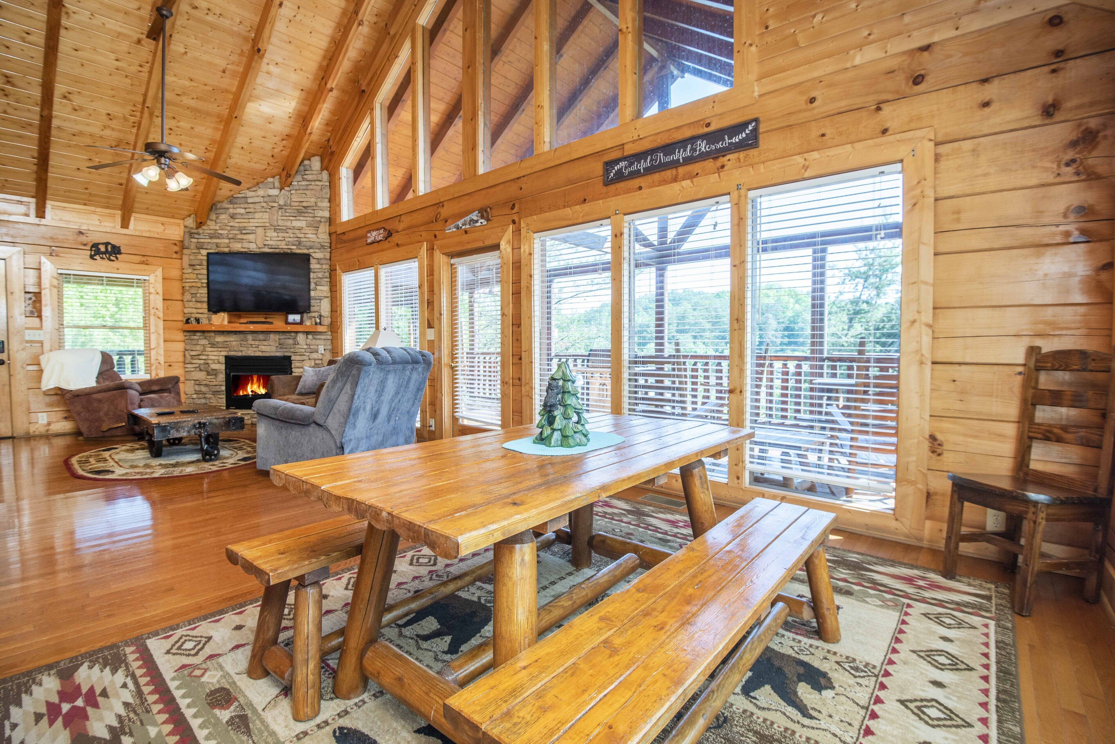 Interno di una baita in legno con camino in pietra, televisore, tavolo da pranzo in legno e una panca.