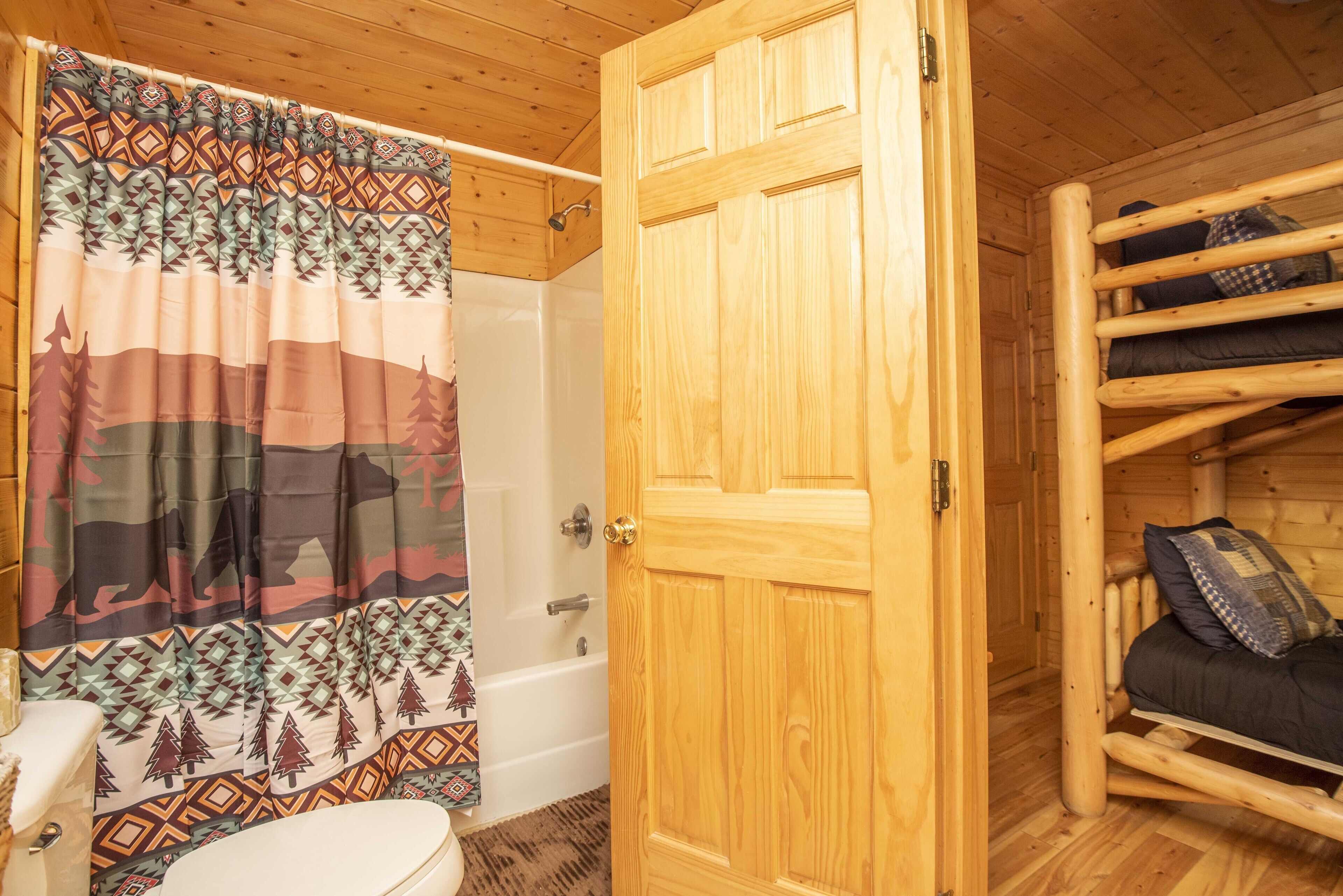 A wooden cabin interior with a bathroom featuring a shower, toilet, and a bed with a headboard.