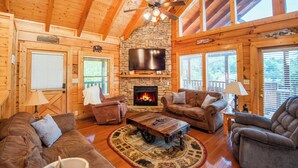 A cozy log cabin interior with a stone fireplace, wooden furniture, and a ceiling fan. - Cozy Smoky Mountain Cabin • Hot Tub, Firepit • 5 Mins to Parkway (Pigeon Forge)