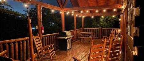 Een houten terras met een barbecue, stoelen en lichtjes.