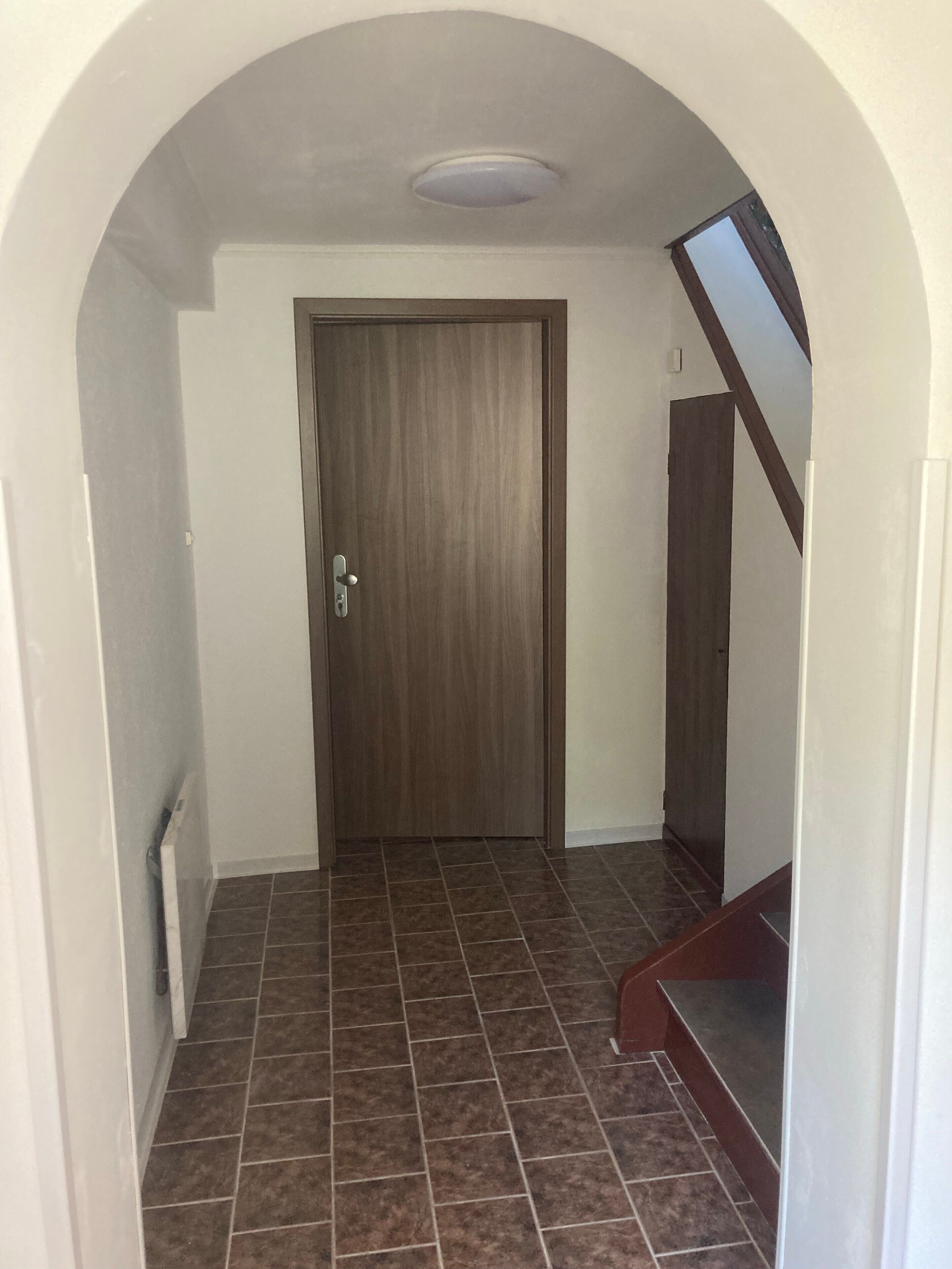 A hallway with a wooden door, tiled floor, and a staircase with a wooden handrail.