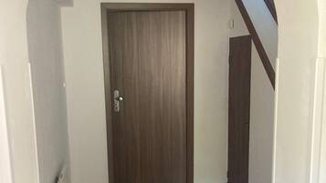 A hallway with a wooden door, tiled floor, and a staircase with a wooden handrail.