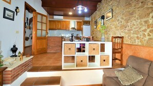 Ein gemütliches Wohnzimmer mit Steinwand, Holzbalkendecke und einer Küchenzeile mit Holzausstattung und Ziegelrückwand.