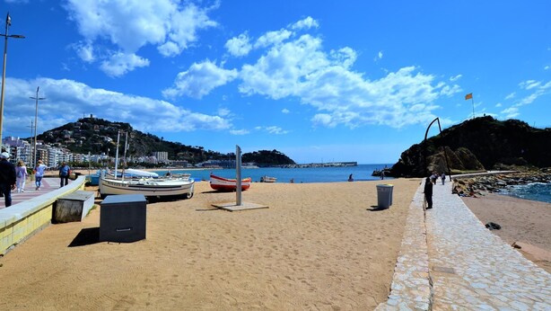 Ein Strand mit Booten, einem Steinweg und blauem Himmel.