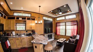 A modern kitchen with wooden cabinets, a marble countertop, and a built-in fireplace. There is a dining area with a sofa and a small table. - Delightful Forest Tiny Home with Hot Tub (Murphy)