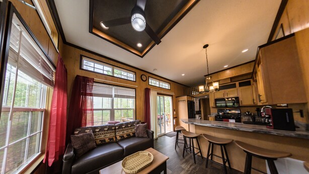 A modern kitchen with a bar area, a dining table, and a sofa in a spacious living area with large windows. - Delightful Forest Tiny Home with Hot Tub (Murphy)