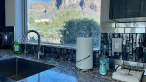 A kitchen with a sink, a glass of water, a paper towel holder, and a view of a mountain. - Beautiful oasis with 40' negative edge pool, swim up bar, hiking in Super. Mtns. (Apache Junction)