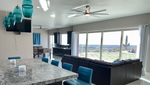 A modern kitchen with a large island, blue bar stools, and a view of a cityscape through large windows. - Beautiful oasis with 40' negative edge pool, swim up bar, hiking in Super. Mtns. (Apache Junction)