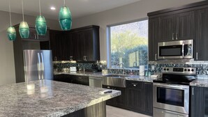 A modern kitchen with dark wood cabinets, stainless steel appliances, a large granite island, and pendant lighting. - Beautiful oasis with 40' negative edge pool, swim up bar, hiking in Super. Mtns. (Apache Junction)