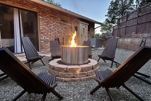 A patio area with a fire pit surrounded by four lounge chairs, a brick wall, and a sliding glass door.