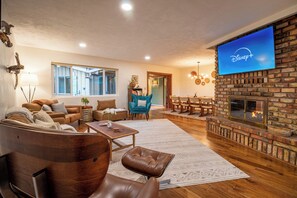 A cozy living room with a fireplace, comfortable seating, and a flat-screen TV displaying Disney+.