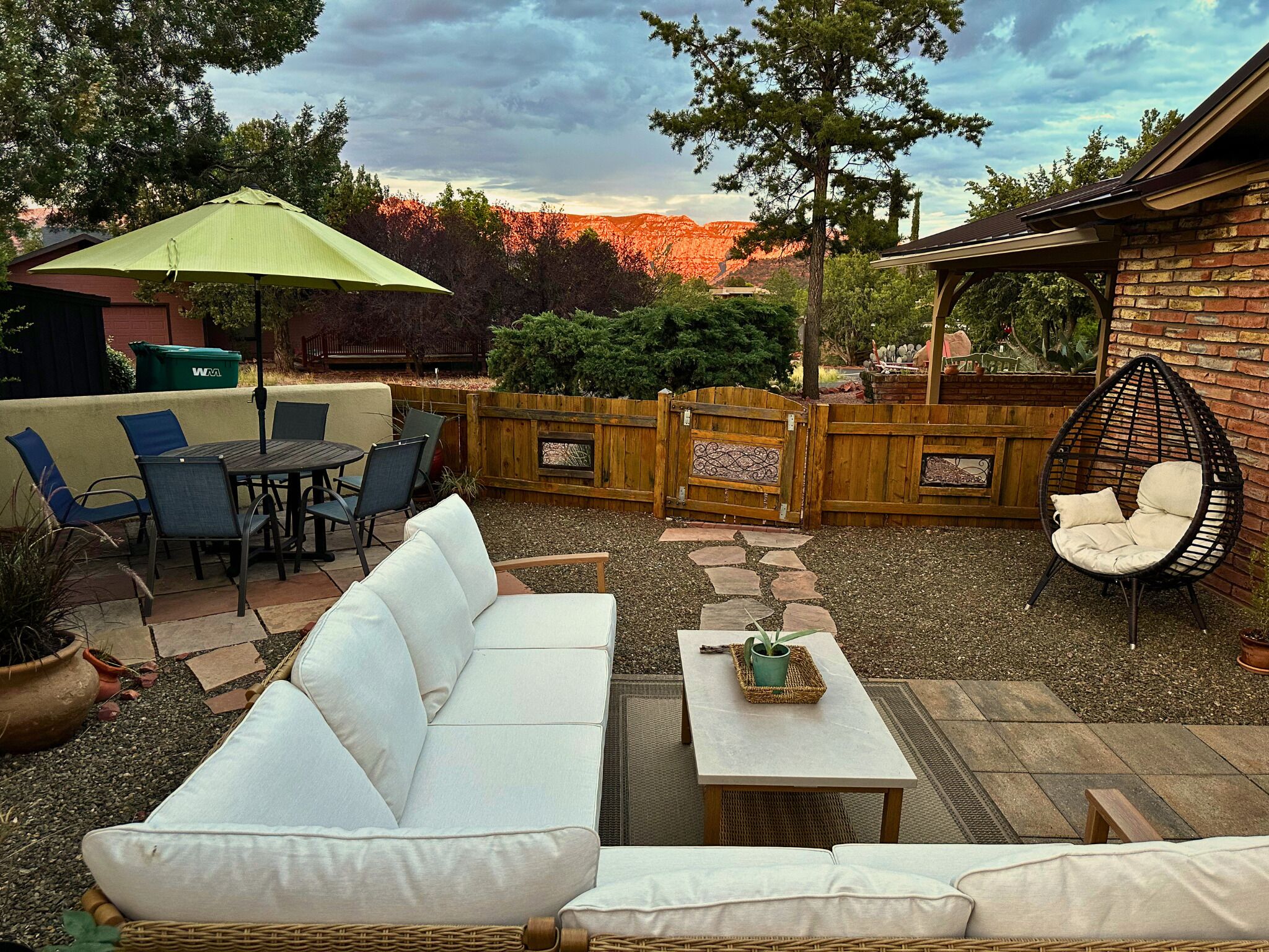 A patio with a white sofa, dining table, chairs, and a hanging chair.
