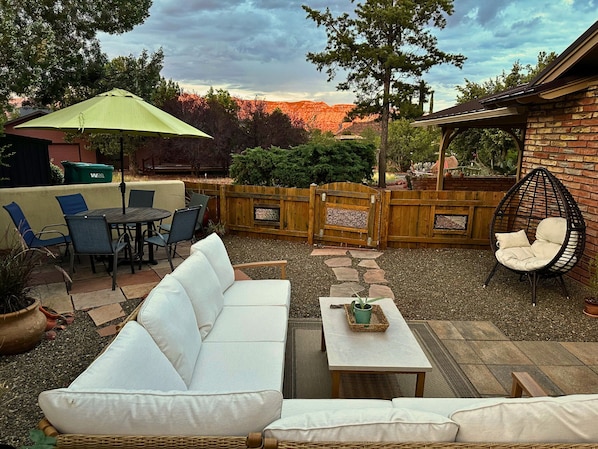 A patio with a white sofa, dining table, chairs, and a hanging chair.