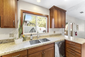 A kitchen with granite countertops, stainless steel appliances, wooden cabinets, and a window with a view of the outdoors.