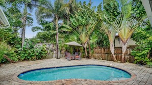 Un jardin à l’arrière de la maison, avec une piscine, entouré d’une végétation tropicale luxuriante et délimité par une clôture en bois.