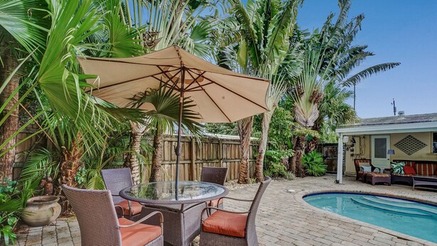 Une terrasse extérieure aménagée avec des meubles en osier, une table ronde en verre et une piscine.