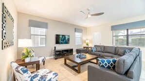 Un salon avec un canapé gris, une table basse, un téléviseur et un ventilateur de plafond.