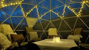 A geodesic dome structure with a table and chairs inside, illuminated by string lights. - 3 bdrm suite w/ rooftop patio, firetable & sauna + hot tub, cold plunge & more! (Kelowna)