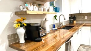 A kitchen with a wooden countertop, a coffee maker, a toaster, and a sink. - 3 bdrm suite w/ rooftop patio, firetable & sauna + hot tub, cold plunge & more! (Kelowna)