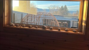 A wooden-framed window with a view of a building and mountains. - 3 bdrm suite w/ rooftop patio, firetable & sauna + hot tub, cold plunge & more! (Kelowna)