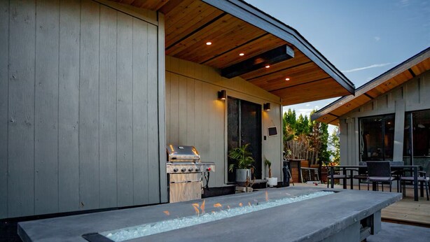 A modern outdoor patio with a built-in grill, seating area, and a water feature. - 3 bdrm suite w/ rooftop patio, firetable & sauna + hot tub, cold plunge & more! (Kelowna)