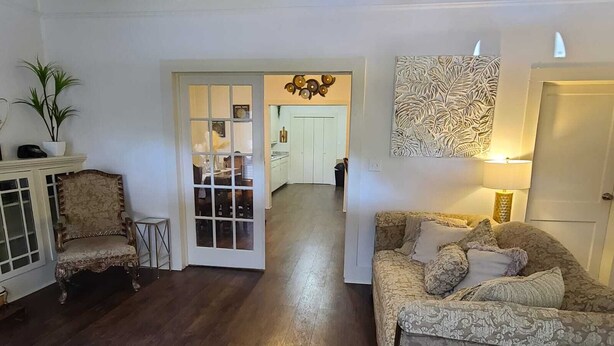 A living room with a patterned sofa, a wooden floor, a white door leading to a kitchen, and a decorative wall piece. - Beautiful 3BR&2BA House located in the Historic part of Brownville-SPI-SpaceX-MX (Brownsville)