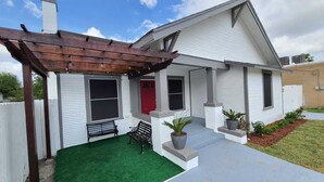 A single-story house with a covered patio, a red door, and a small front yard with artificial grass and potted plants. - Beautiful 3BR&2BA House located in the Historic part of Brownville-SPI-SpaceX-MX (Brownsville)