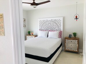 Ein Schlafzimmer mit einem Bett, einem Deckenventilator und zwei Nachttischen mit dekorativen Paneelen.