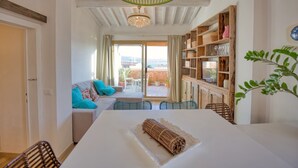 Un salon moderne avec un canapé blanc, des coussins turquoise, une table à manger sur laquelle est posé un tapis enroulé, et une bibliothèque en bois.