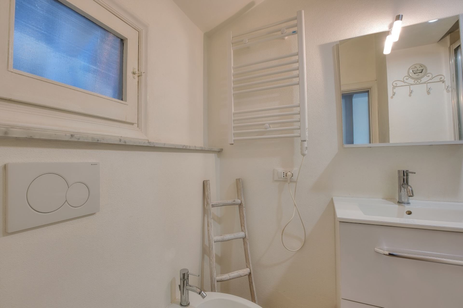 A bathroom with a toilet, sink, mirror, towel rack, and a window with blinds.