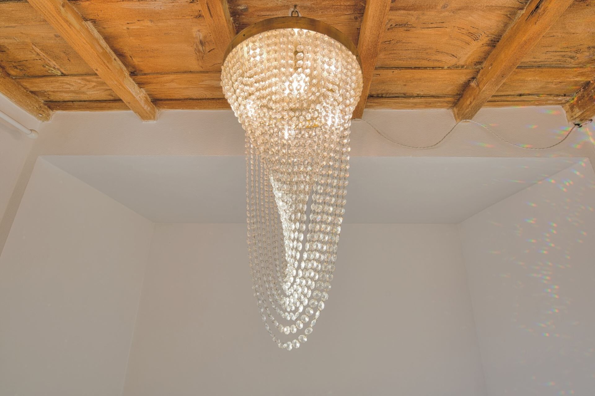 A chandelier with multiple tiers of clear crystals hanging from a wooden ceiling.