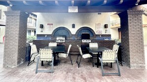 An outdoor patio with a grill, seating, and a covered area with a sign indicating a 24-person spa capacity. - Resort Style Condo near Disneyland, Beaches, Los Angeles & so much more  (Fountain Valley)