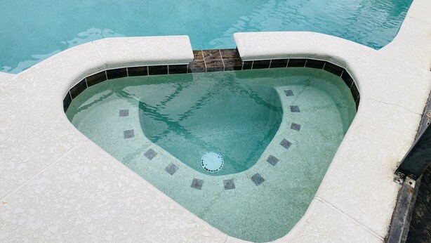 A heart-shaped hot tub with a tiled edge, surrounded by a pool.