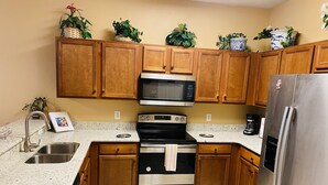 A kitchen with wooden cabinets, a stainless steel refrigerator, a microwave, an oven, and a sink.