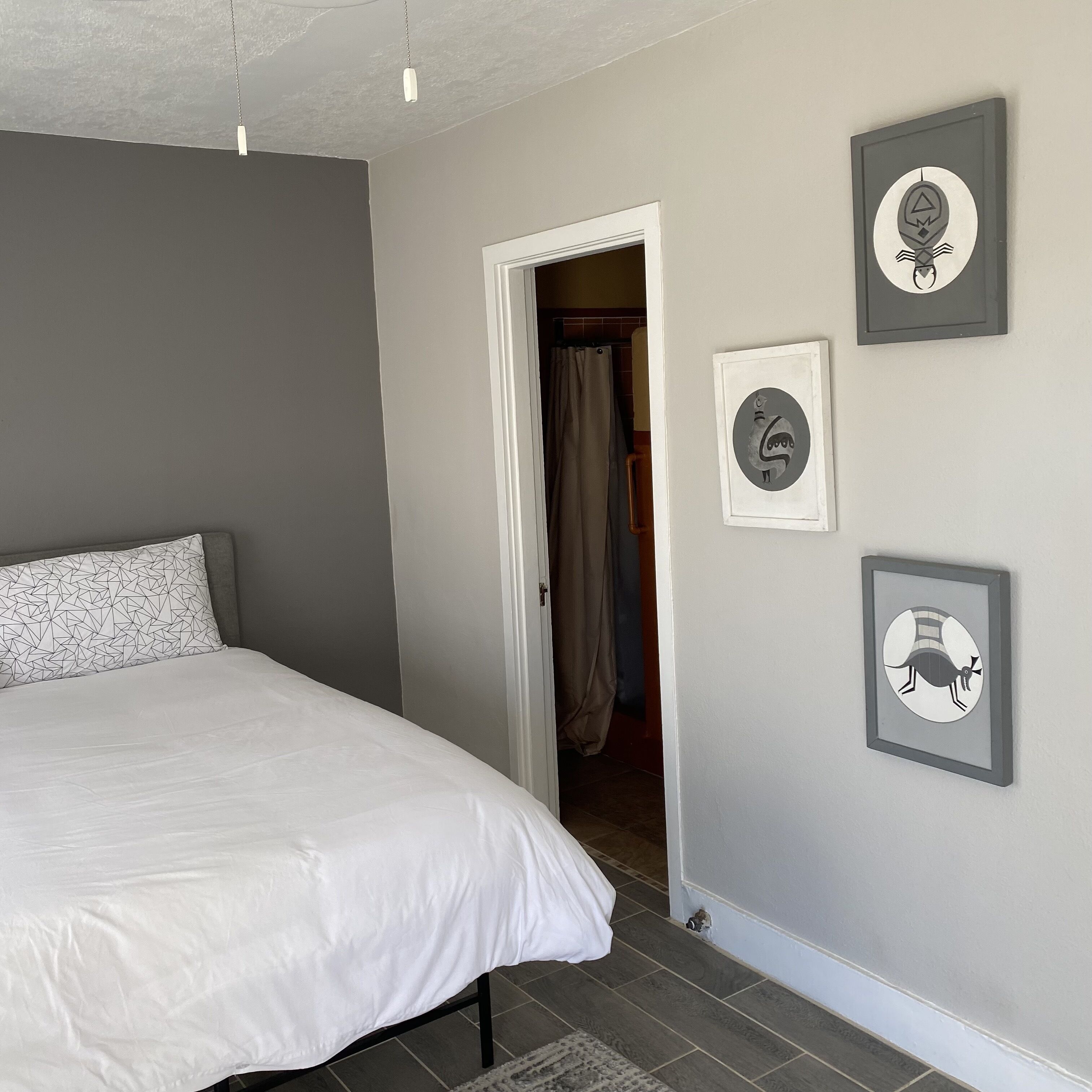 A bedroom with a bed, a door leading to a bathroom, and three framed pictures on the wall.