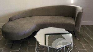 Un salon moderne avec un canapé gris aux lignes courbes, une table basse en verre et une œuvre d’art abstraite encadrée accrochée au mur.
