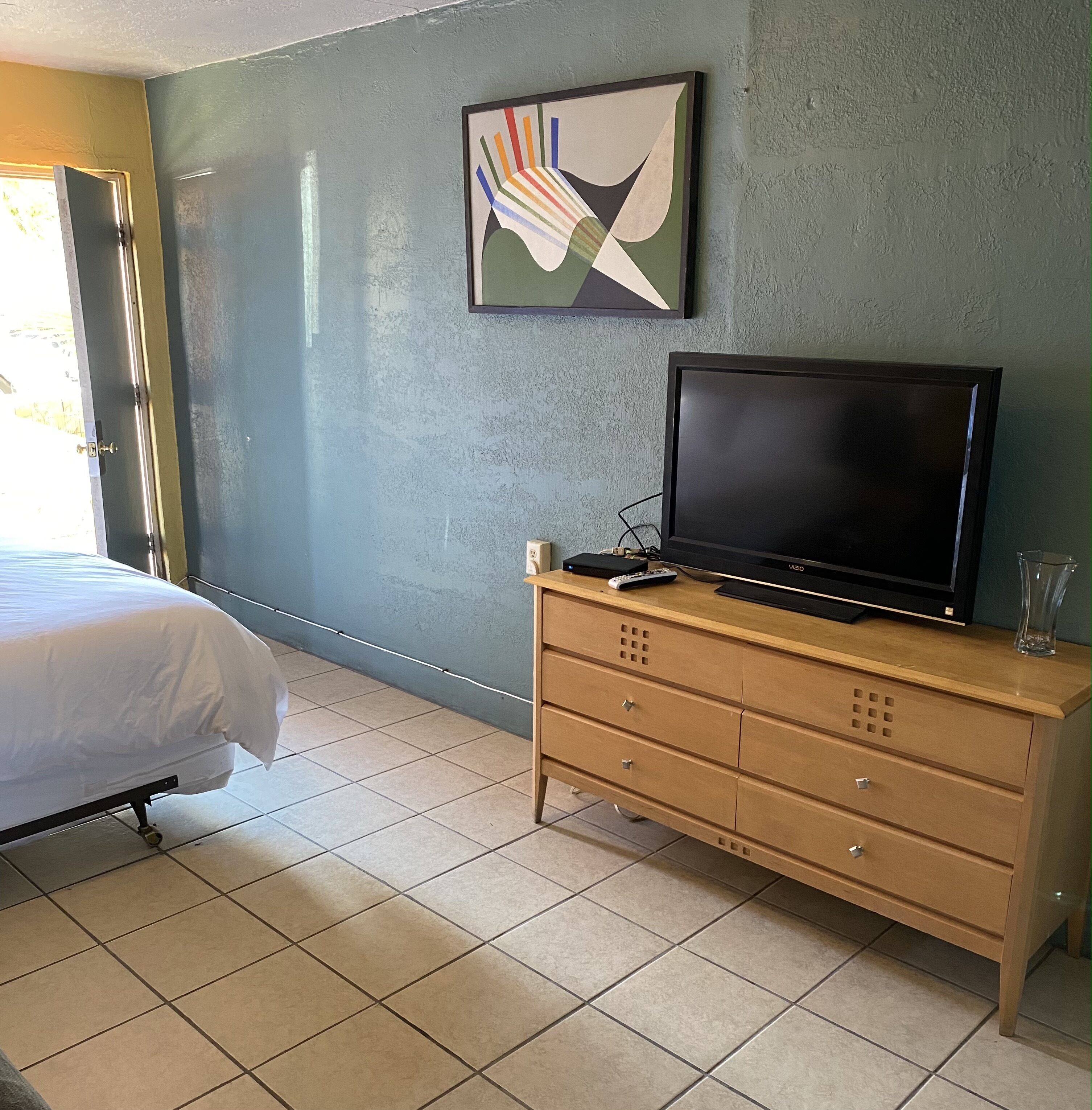 A hotel room with a bed, a TV on a wooden dresser, and a painting on the wall.