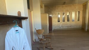 Une pièce spacieuse dotée d’un plancher en bois, d’un ventilateur de plafond, d’un tapis à motifs zébrés, d’un fauteuil à bascule et d’une robe blanche suspendue à un porte-vêtements.