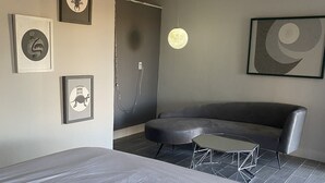 Une chambre d’hôtel moderne dotée d’un grand lit, d’un coin salon avec un canapé et une petite table, et d’œuvres d’art accrochées aux murs.