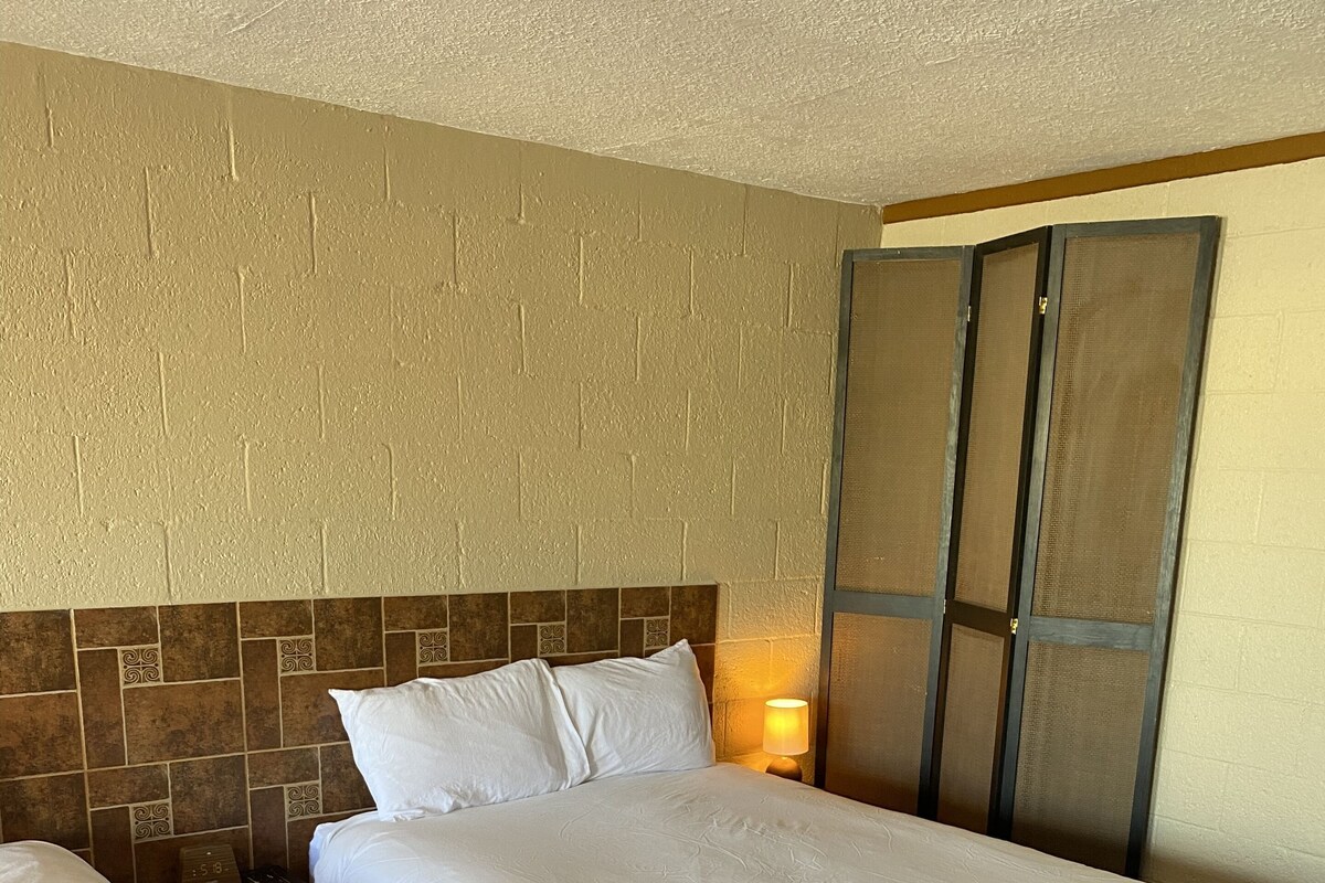 A hotel room with two single beds, a wooden floor, a brick-patterned wall, and a sliding door.
