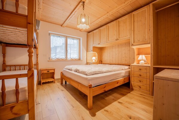 Une chambre à coucher en bois, avec un lit, une table de chevet, une commode et une fenêtre avec des rideaux.