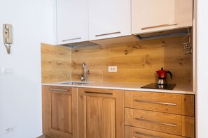 A kitchen with wooden cabinets, a white countertop, a stainless steel sink, and a red kettle.