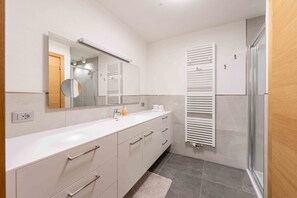 A modern bathroom with a white vanity, a mirror, a towel rack, and a shower area. - Parco Canazei - Casa al Parco Deluxe (Canazei)