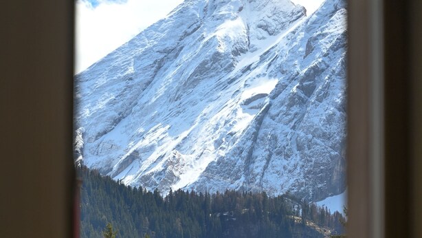 Une fenêtre donnant sur une montagne enneigée et une vallée boisée.