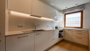 Une cuisine moderne avec des meubles blancs, un évier en acier inoxydable et une fenêtre équipée de stores.