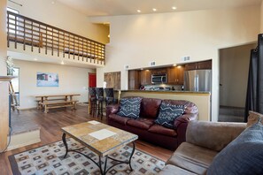 A spacious living area with a wooden floor, a leather sofa with patterned cushions, a glass coffee table, and a dining table.
