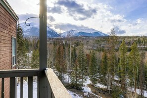 A wooden cabin with a balcony overlooking a snowy mountain landscape and a forest.