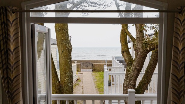 Ein überdachter Außenbereich mit Holzdeck, weißen Geländern und Blick auf das Meer.